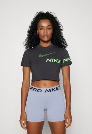 T-shirt nera corta Nike con logo verde, abbinata a pantaloni corti a vita alta di un leggero color viola con una vita brandizzata nera.