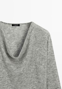 Lichtgrijze gebreide trui met een gedrapeerde col als halslijn en lange mouwen, waarbij de bovenkant van de voorkant en het label aan de binnenkant van de kraag zichtbaar zijn.