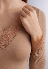 Top de manga larga beige con escote en V adornado con delicado encaje. La tela parece suave y con una textura lisa.