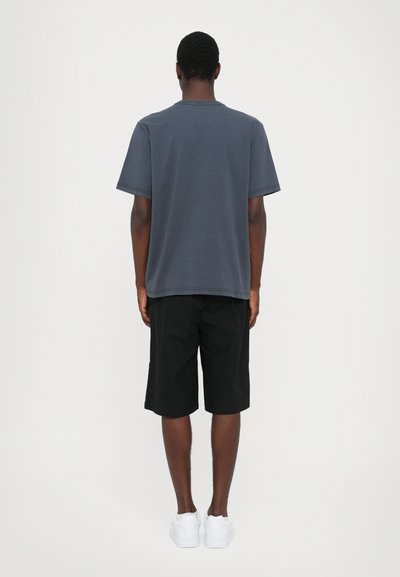 Tmavě šedé bavlněné tričko krátkým rukávem, zkombinované s černými šortkami. Outfit doplňují bílé tenisky. Jednoduché, volné střih.