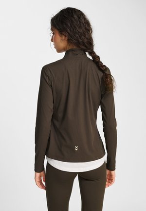 Olivegrünes Langarmshirt mit hohem Kragen, gerippter Textur, subtiler Markenaufführung auf der Rückseite und über einem weißen Shirt getragen.