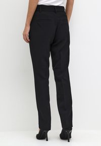 Black tailored pants made of smooth fabric, featuring a slim fit, back pockets, and a mid-rise waist. Worn with black heels.