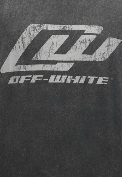 Φθαρμένο λευκό γεωμετρικό λογότυπο και κείμενο "OFF-WHITE" τυπωμένα σε ξεθωριασμένο μαύρο ύφασμα.
