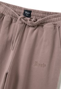 Pantalones de chándal de color malva claro con cinturilla elástica y cordón. Cuenta con la palabra 'Utopia' bordada en un color a juego, de textura suave.