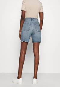 Högmidjade blå denimshorts med fransad nederkant, femficksdesign och ljus tvätt, parat med vita sneakers.