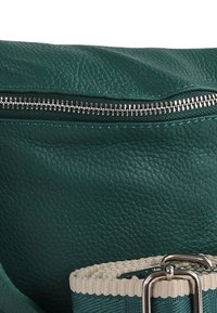 Turkooise leren tas met een gestructureerde afwerking, voorzien van een zilveren rits en een lichtgekleurde, gevlochten band met een metalen gesp.