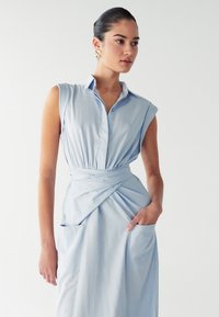 Hele sinine särgkleit lühikeste varrukatega, nööbid üles kaelus ja vööga ümbertõmmatav disain. Omab kaht küljetaskut ja sujuvat kangatekstuuri.