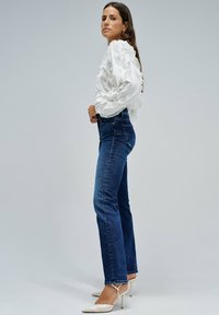 Blusa blanca, texturizada, de manga larga con mangas abullonadas, combinada con jeans de pierna recta de cintura alta en azul oscuro y tacones blancos puntiagudos.