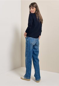 Marineblauwe top met lange mouwen en aansluitende mouwen, gecombineerd met lichtblauwe hoge taille jeans met zijzakken en een relaxte pasvorm. Crème sneakers.