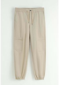 Pantalon de jogging beige avec taille élastique, fermeture à cordon, poches latérales et poignets élastiques. Texture lisse et design à coupe décontractée.