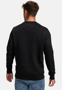 Felpa nera realizzata in un tessuto morbido, con scollo rotondo e maniche lunghe. Il retro presenta una texture liscia e un design semplice.