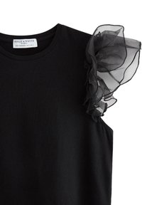 Sort bomuld t-shirt med en gennemsigtig sort flæsedetalje på den ene skulder. Rund halsudskæring, korte ærmer, glat tekstur, minimalistisk design.