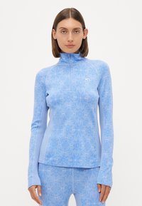 Ανοιχτό μπλε αθλητικό τοπ με σχέδιο μισού φερμουάρ, μακριά μανίκια, υφή από ελαστικό ύφασμα και διακριτό γεωμετρικό μοτίβο.