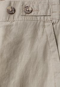 Tissu en lin beige avec deux boutons marbrés marron et crème et une couture détaillée près d'une ceinture et du bord d'une poche.