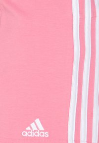 Pantalones cortos deportivos rosa con una textura suave, rayas blancas en los costados y un pequeño logo blanco de adidas en la esquina inferior izquierda.