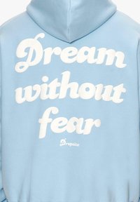 Hellblaue Kapuzenjacke mit weißem Text, der "Traum ohne Angst" liest, und einem kleinen Logo "Dropsize" am unteren Rand. Weicher Stoff, lockere Passform.