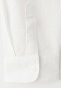Poignet de chemise blanche à manches longues avec un seul bouton blanc et des détails de couture visibles sur le tissu.