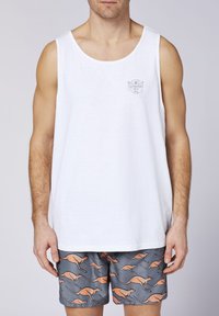 Weißes Baumwoll-Top mit rundem Ausschnitt, ausgestattet mit einem kleinen grafischen Logo auf der Brust. Kombiniert mit grauen Badehosen, die orangefarbene Känguru-Muster zeigen.