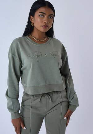 Sweatshirt court vert olive avec texte brodé, accompagné d'un jogging assorti. Texture douce, col rond et coupe décontractée.