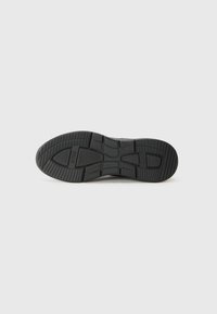 Suela de zapato de goma negra con un diseño de banda de rodadura estampado. Presenta surcos y áreas elevadas para una mejor tracción, con la marca emblema visible.