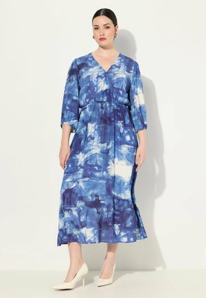 Blaue und weiße Batik-Midaxi-Kleid mit V-Ausschnitt, drei Viertelärmeln und elastischem Taillenbund. Getragen mit weißen High Heels.