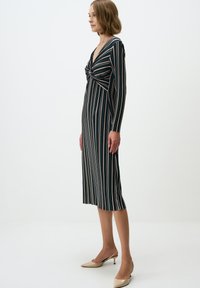 Gestreiftes, langärmliges Kleid mit tiefem V-Ausschnitt und Knoten-Detail an der Brust. Das Muster umfasst dunkelgrüne, rosa und weiße Streifen.
