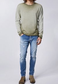 Světle olivově zelený gradientový sweatshirt s kulatým výstřihem, lehký materiál, kombinovaný se světle modrými roztrhanými džíny a béžovými kotníkovými botami.