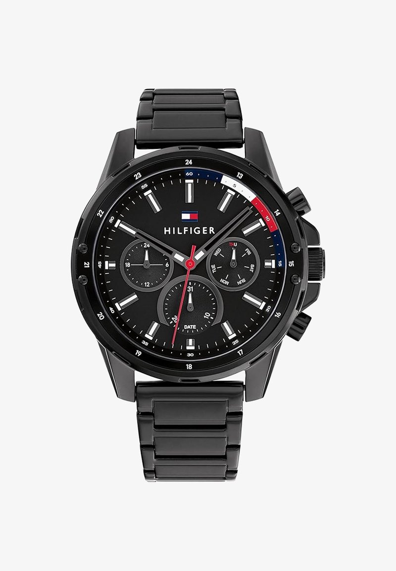 Montre-bracelet noire Tommy Hilfiger avec bracelet en métal, trois sous-cadrans pour 24 heures, jour et date, et aiguille des secondes rouge pointant sur 6 secondes.