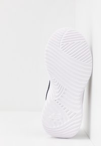 Semelle de chaussure en caoutchouc blanc texturé, présentant des motifs de traction ondulés et un petit logo sur le talon. La couleur contraste avec la tige de la chaussure.