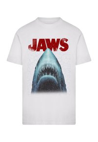 T-shirt blanc avec un graphisme de la gueule ouverte d'un requin et le texte "JAWS" en rouge vif. Le design comprend une texture craquelée en arrière-plan.