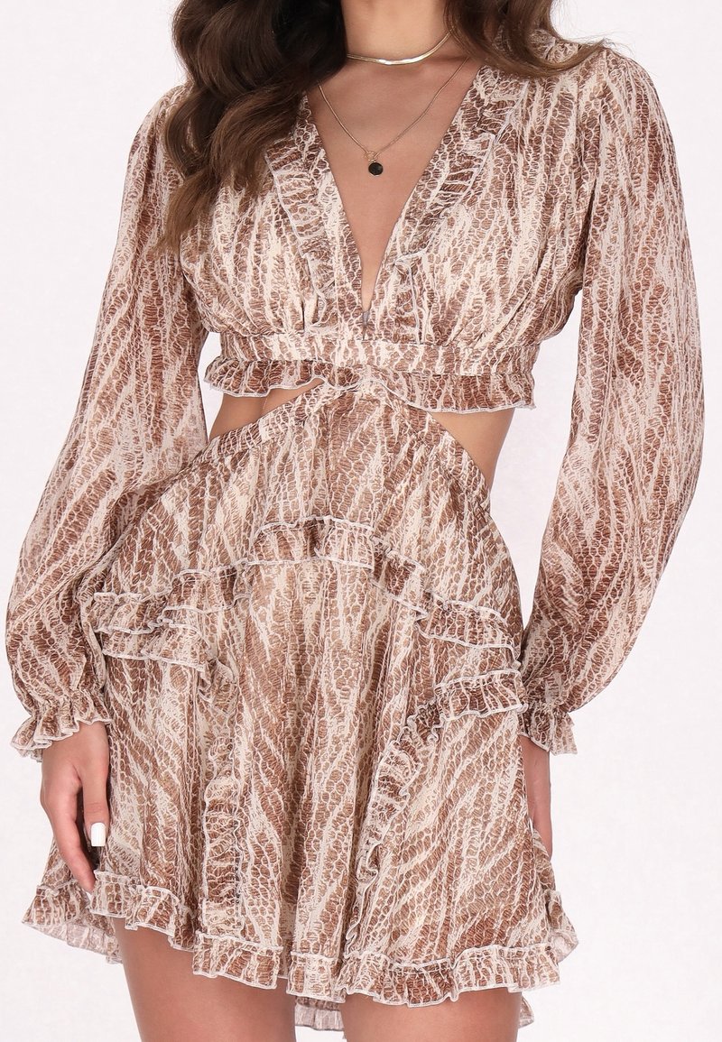 Robe à manches longues, imprimé serpent marron et beige, col en V profond, taille découpée, bordure à volants et jupe fluide portée par une femme avec des colliers superposés.