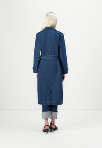 Jeansjakke med belte i livet, lange ermer og stor krage. Blå farge med lys søm. Har rett skjæring og baksplitt.