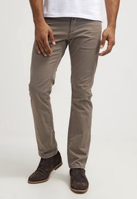Lichtbruine katoenmix chino's met een slim fit, voorzien van subtiele stiksels, zijzakken en gedragen met donkerbruine suède enkellaarsjes.