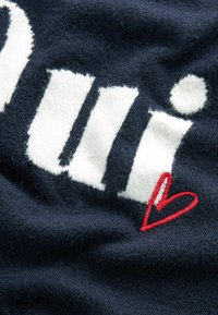 Tissu en maille bleu marine avec de grandes lettres blanches audacieuses et un accent de cœur brodé rouge, présentant une texture douce et un design en couches.