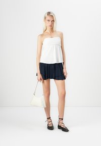 Top bez ramínek v bílé barvě, rozšířená námořnická sukně s volánky, černé lace-up baleríny a bílá taška s akcentními stehy. Minimalistický design.