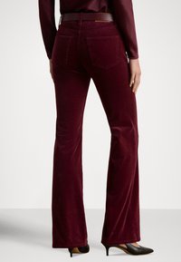 Bordowe sztruksowe spodnie dzwony o fakturowanej powierzchni, z dwoma tylnymi kieszeniami i ciemnobrązowym paskiem, w zestawieniu z czarnymi butami na wysokim obcasie.