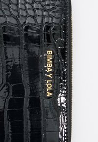 Juodas patentuotas krokodilo odos raštas, su auksiniu "BIMBA Y LOLA" logotipu, užtrauktuku ir tekstūruota paviršiumi su išskirtiniais raštais.