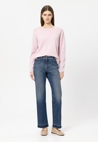 Hellrosa Pullover mit Rundhalsausschnitt, kombiniert mit dunkelblauen, gerade geschnittenen Jeans mit ausgefranstem Saum und beigen, gewebten Slippern.