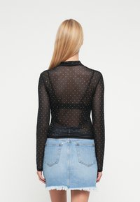 Sort gennemsigtig langærmet top med sølvprikket mønster, kombineret med en lyseblå denim mini nederdel med frynset kant og baglommer.