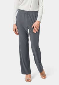 Grijze, lichte broek met elastische tailleband en een rechte pijp. Gecombineerd met een witte lange mouw top en beige sandalen.