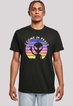 Black cotton t-shirt featuring a graphic of an alien with a peace sign against a rainbow-striped background. Text reads "I COME IN PEACE."