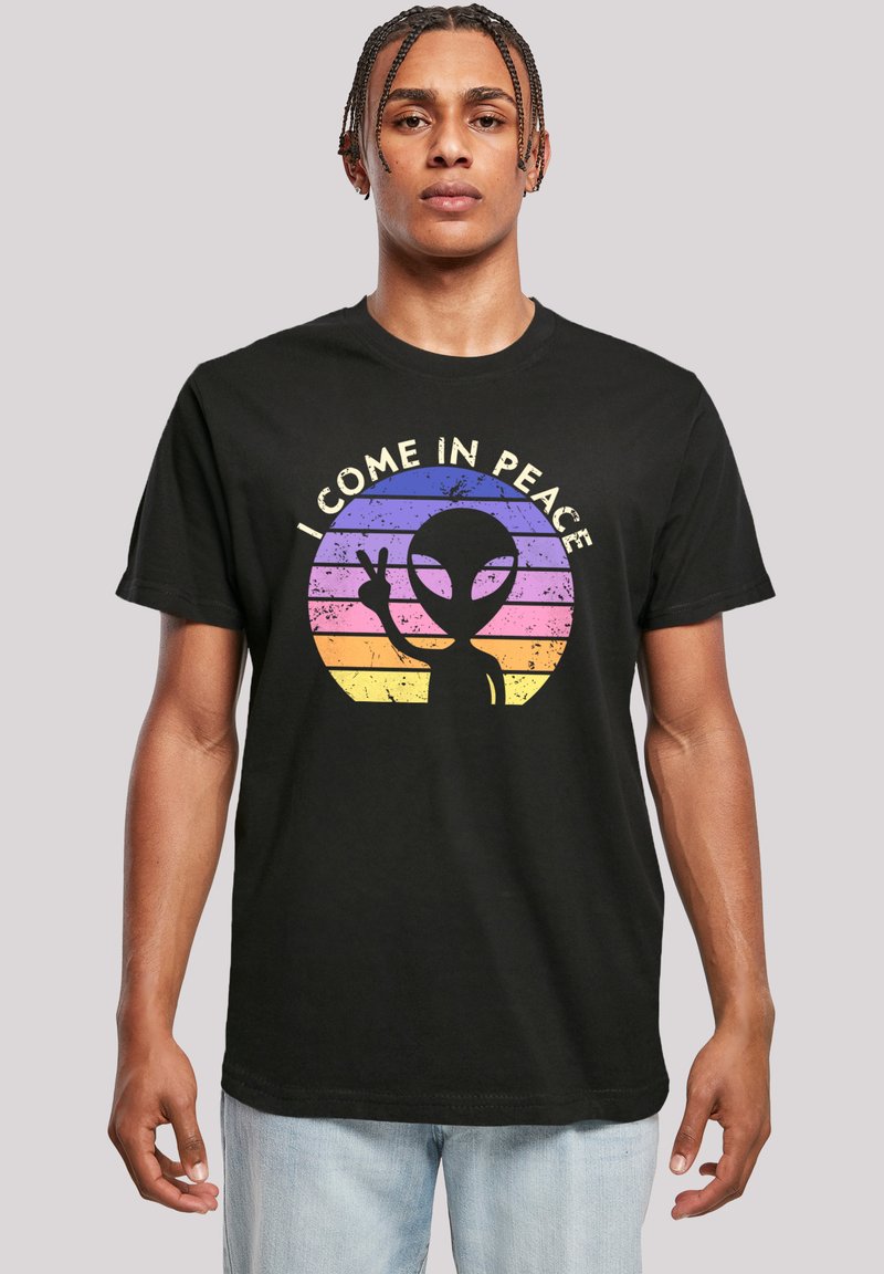 Black cotton t-shirt featuring a graphic of an alien with a peace sign against a rainbow-striped background. Text reads "I COME IN PEACE."