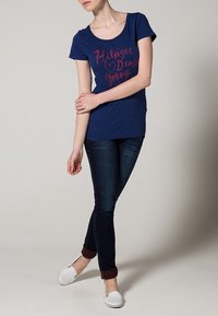 Mörkblå kortärmad t-shirt med rund halsringning och rosa text. Matchas med mörka jeans och vita slip-on skor.