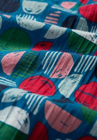 Textil con fondo azul y patrones geométricos coloridos en rojo, verde, rosa y blanco. La tela tiene un acabado texturizado.