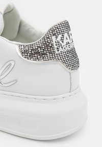 Hvite skinnsneakers med teksturert sølvakcent på hælen som har rhinestones. "KARL LAGERFELD" logo preget på siden.