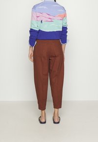 Stickad tröja med ett färgglatt landskapsmönster i blått, rosa och lila, i kombination med högmidjade byxor i rostfärg och sandaler.