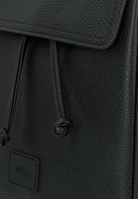 Mochila de cuero negro con una superficie texturizada, cierre de cordón y una etiqueta rectangular con el nombre de la marca.