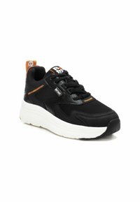 Zapatilla deportiva negra con una parte superior texturizada y paneles de malla, costuras en contraste de color naranja y una suela de goma blanca.
