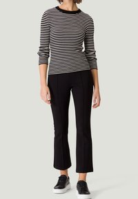 Czarna i biała koszula w paski z długim rękawem i okrągłym dekoltem, zestawiona z czarnymi dopasowanymi spodniami i czarnymi tenisówkami z białymi podeszwami.