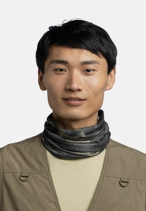 Young man with short black hair wearing a beige vest, light shirt, and dark patterned neck gaiter, facing forward against a plain background.